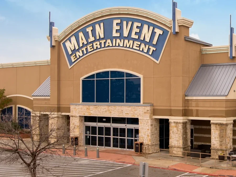 Main Event Entertainment storefront with tan stucco walls, stone columns and a blue arched sign above the entrance