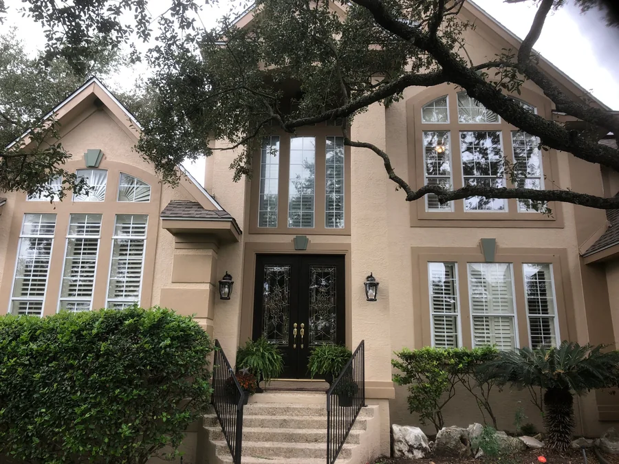 Two story stucco home under a live oak with arched windows, sage keystone accents and dark double entry doors, repainted by Value House Painting